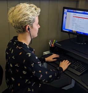 Person wears under the chin headphones as they type on the computer.